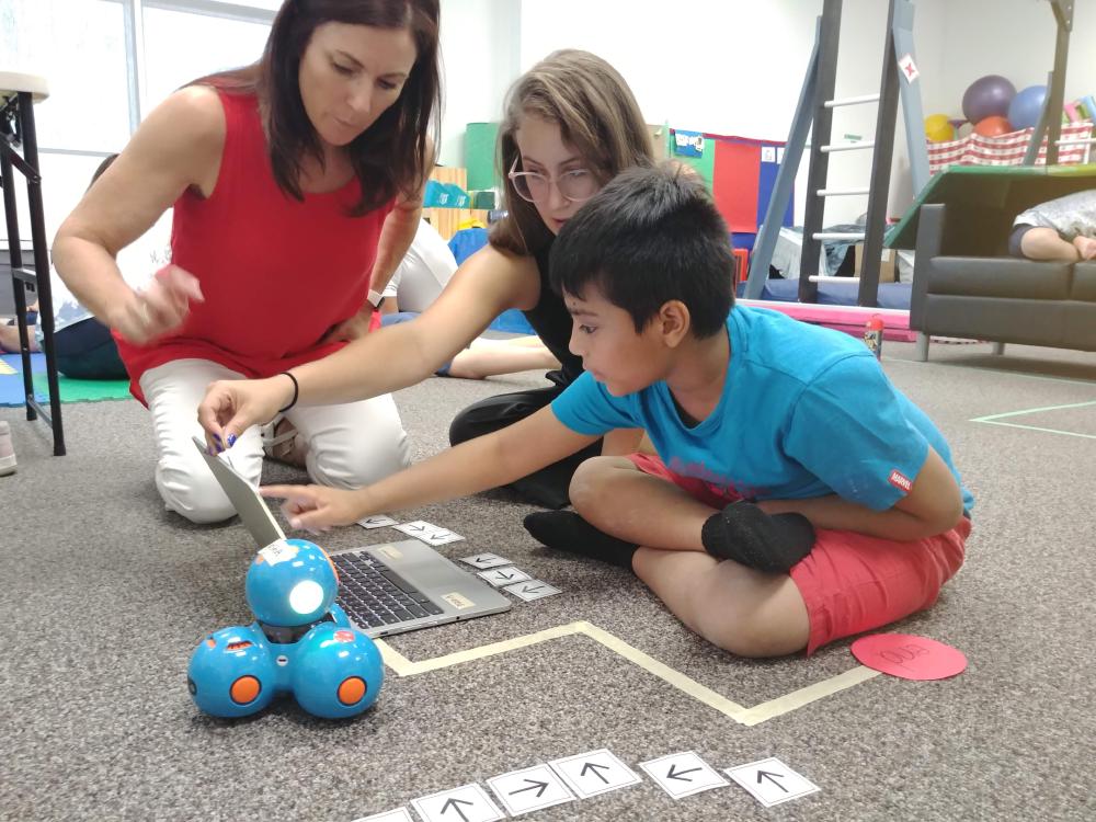 Two instructors working with a kid on a laptop to build a program sequence for the robot Dash