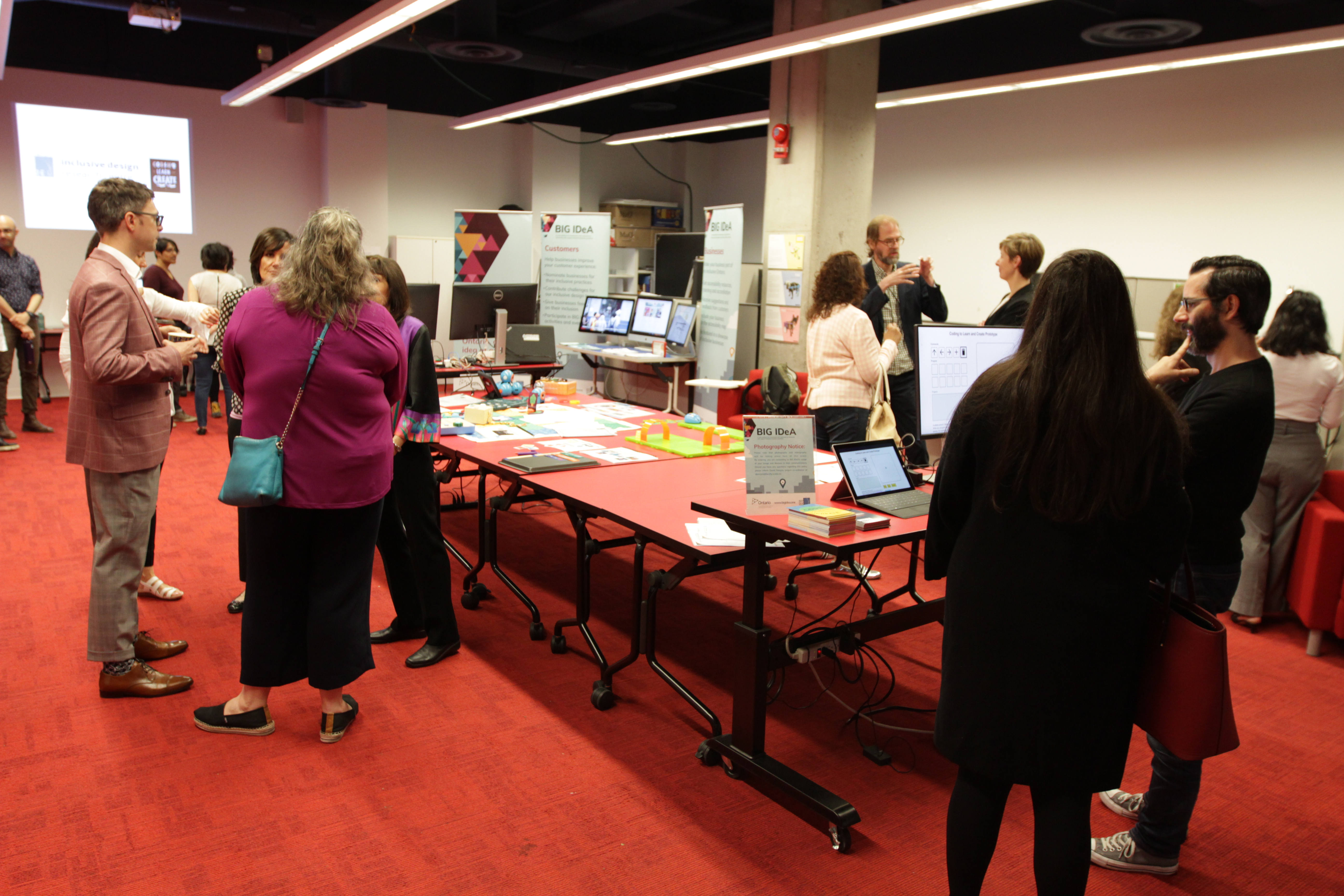 Several groups of people cahtting at different exhibit stations in a large room. 