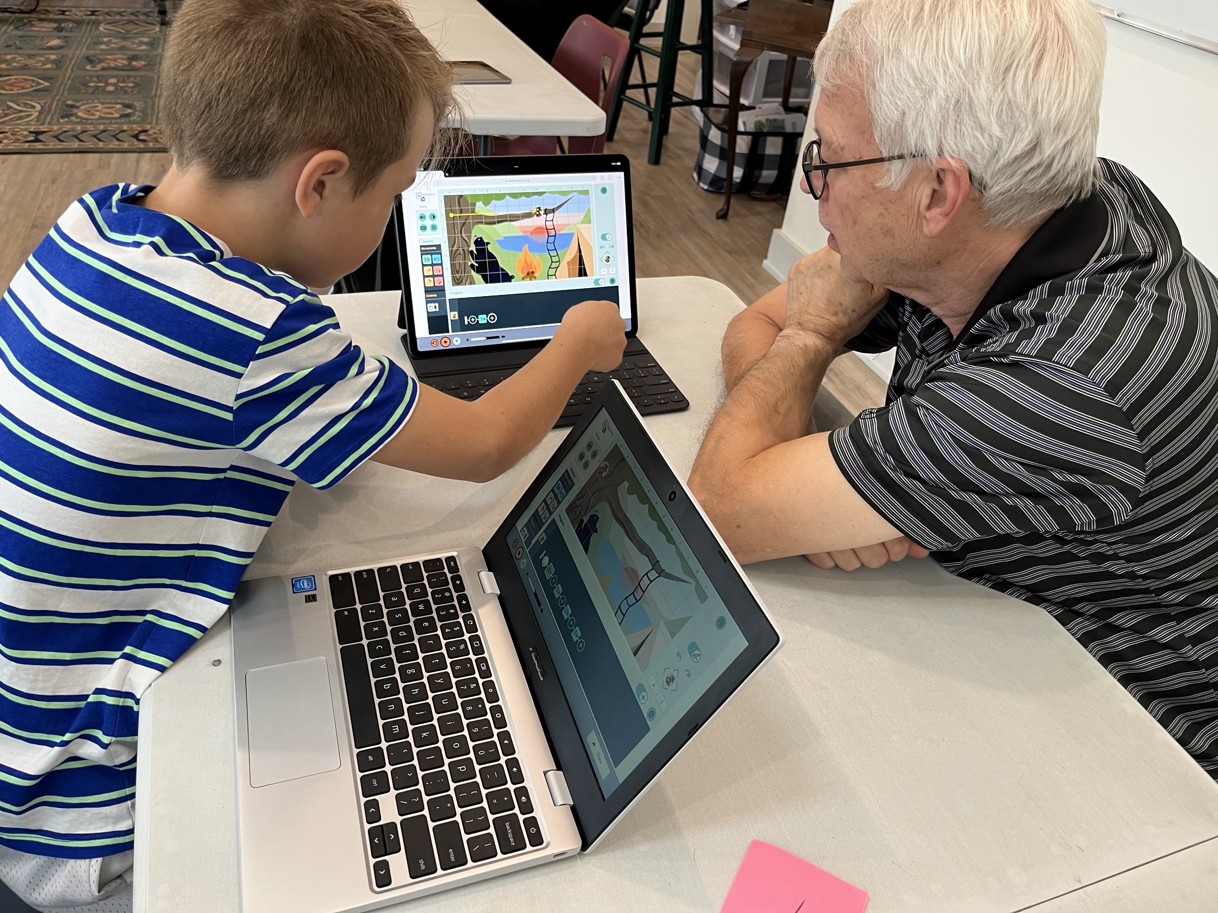 Young student showing an adult how to use Weavly coding environment on a laptop. 