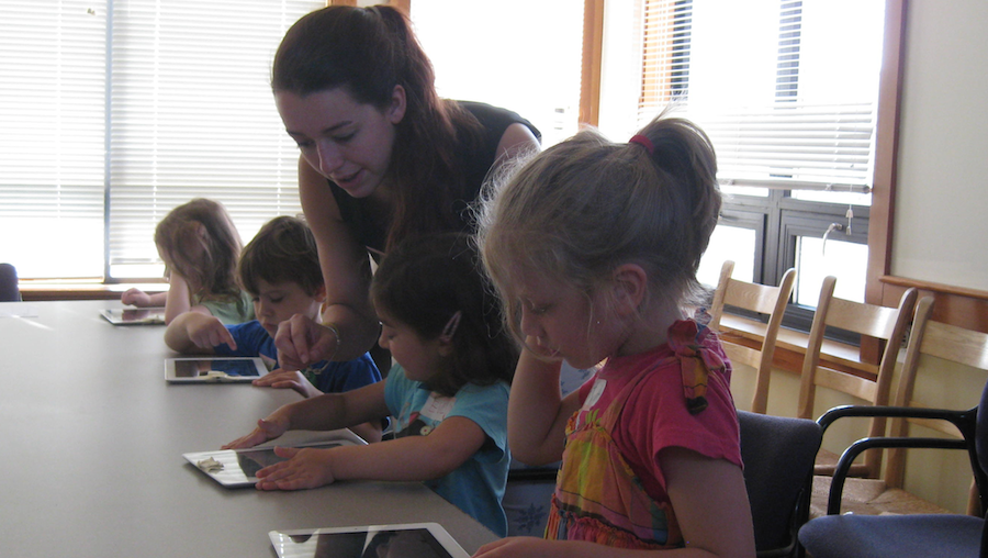 An instructor is helping young children to work with ScratchJr on their tablets.